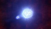 On a dark hazy background two bright objects appear in the centre. On the left, a small, purple-white disc-shaped object is surrounded by wisps. These wisps connect to a larger, brighter, blue-white circular object.