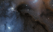 This image shows dark brownish clouds, on the right, and glowing bluish ones, on the left, both over a starry background. Among the stars, a few of them are much brighter and bigger than the others.