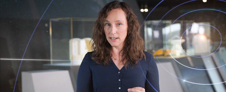 This image shows a screen capture from the promotional material for the first episode of Chasing Starlight. The host, Suzanna Randall, stands in the middle of the image wearing a dark blue shirt. One of her hands is resting on a surface in front of her, while the other is held pensively. On the right of the image blue concentric circles radiate outwards.