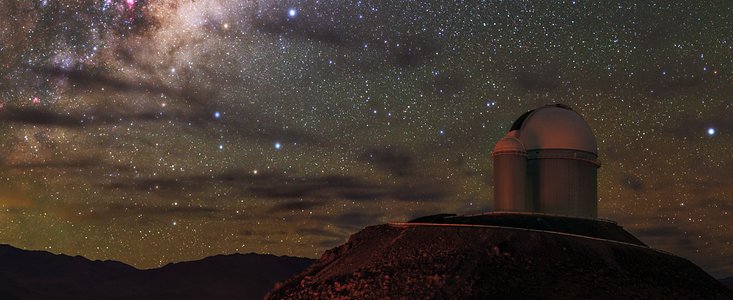 The radiant purple and white Milky Way dominates the star-speckled sky in this image, as it stretches from the top right of the frame to the bottom left. In the bottom right of the image, a telescope with its characteristic white dome examines the sky above from its perch at the top of a hill.