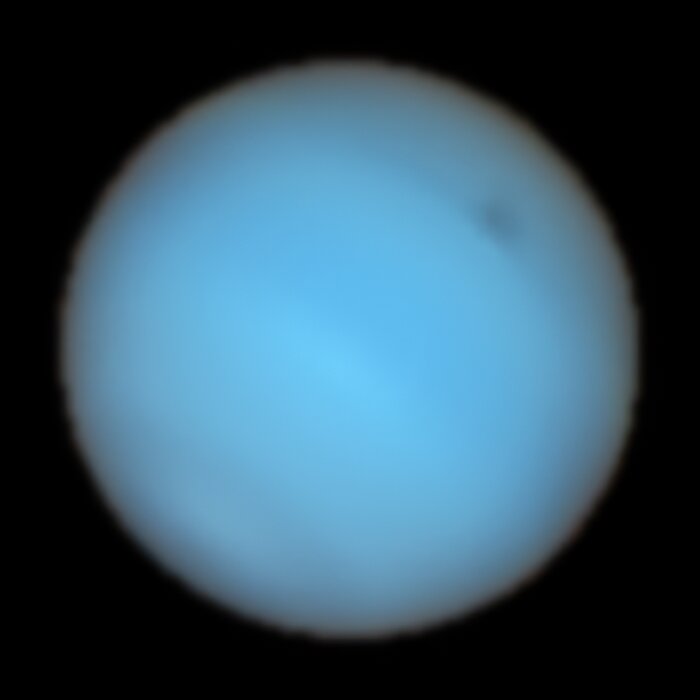 Ein Teleskopbild des Planeten Neptun. Es handelt sich um eine fast eigenschaftslose blaugrüne Scheibe mit einem schwachen dunklen Fleck oben rechts.
